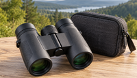 Prismáticos compactos con su funda sobre una mesa de madera y paisaje natural al fondo Prismáticos compactos con su funda sobre una mesa de madera y paisaje natural al fondo